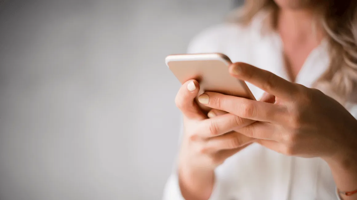 Kobieta w białej koszuli korzysta z telefonu, przeglądając ofertę pożyczki online.